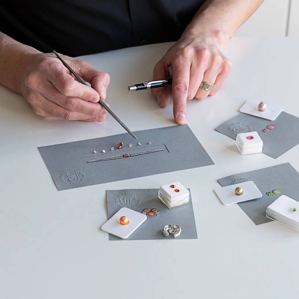 Designer with jewellery designs and matching stones on the table in front of him